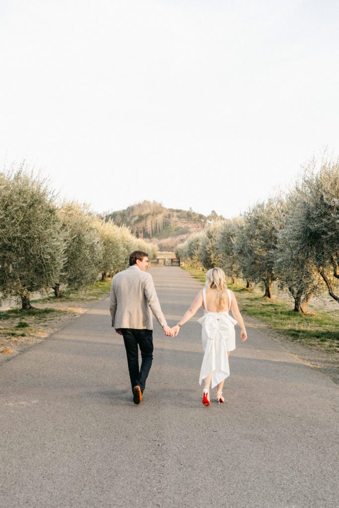 bride and groom walk hand in hand down path with olive trees