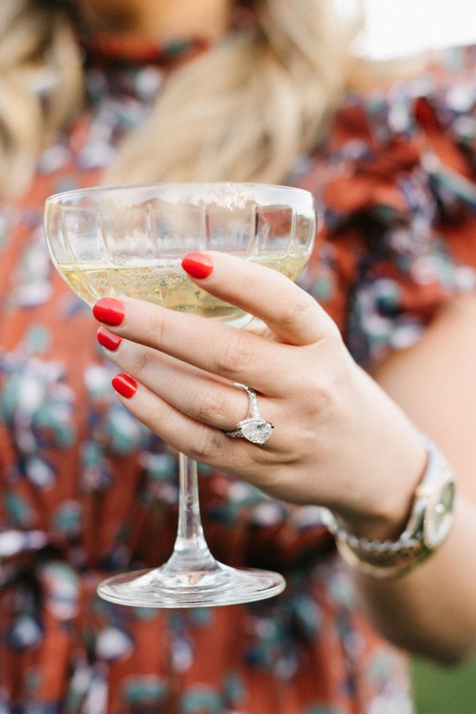 bride holds champagne glass while wearing custom 3.5 carat pear cut diamond engagement ring