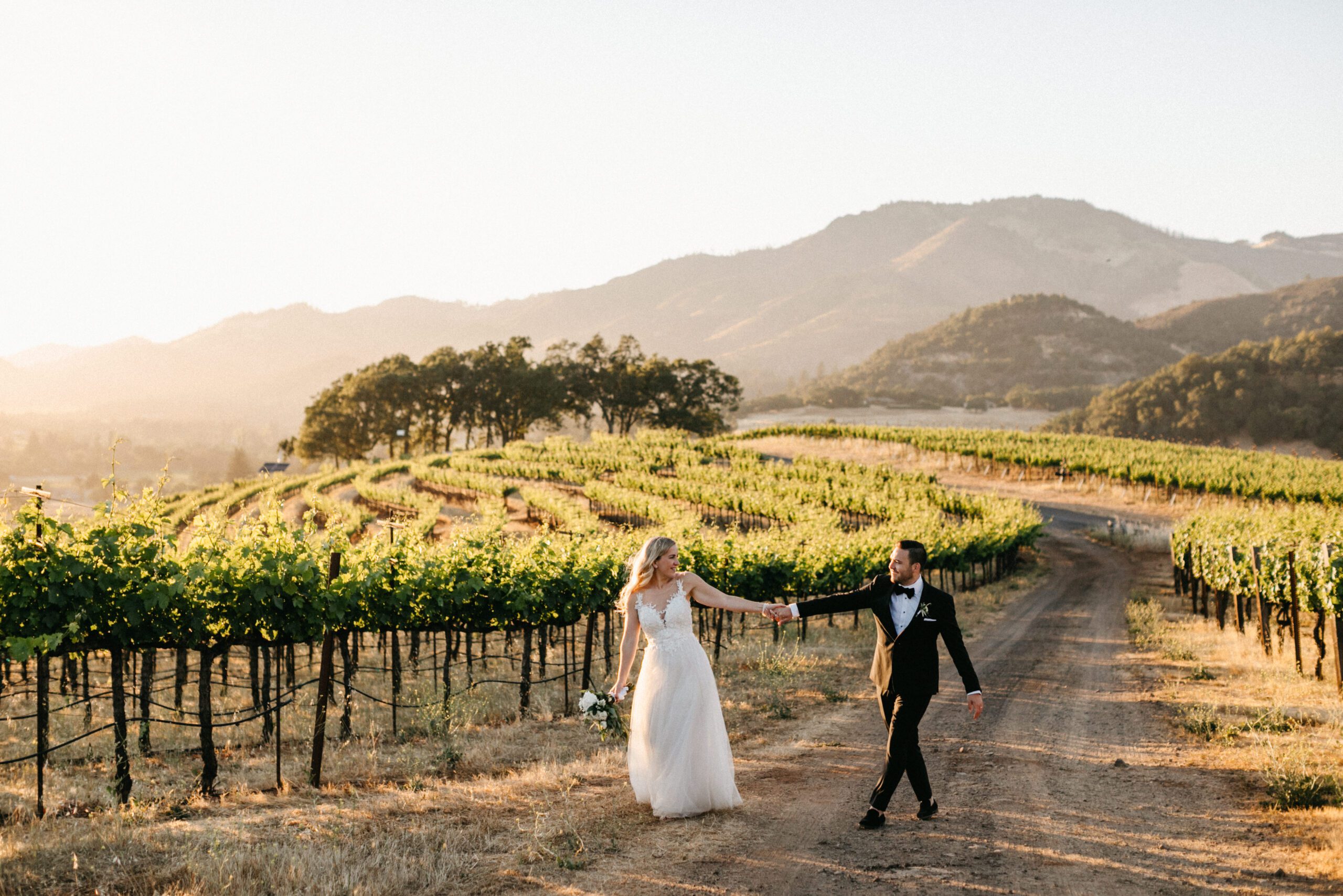 bride and groom walk during sunset and golden hour portraits on boot hill at kunde family winery for their wedding, vineyards in background